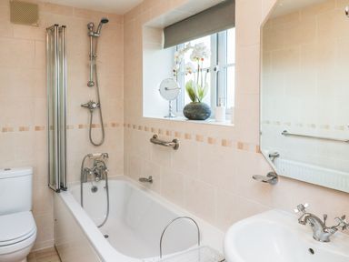 A bathroom with a bathtub shower toilet sink mirror and a window with flowers at South Lodge Hazelbury Bryan