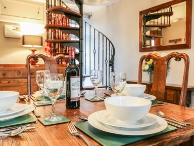A dining room with a wooden table set with white bowls plates wine glasses and a bottle of wine near a spiral staircase at South Lodge in Hazelbury Bryan