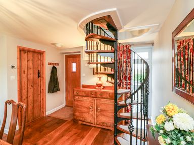 A room with a wooden spiral staircase a wooden sideboard with a lamp wooden doors and a floral arrangement at South Lodge in Hazelbury Bryan