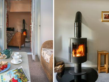 A modern wood burning stove with a fire inside next to a basket of logs and a small wooden table and a view into a living room with a brown sofa at South Lodge in Hazelbury Bryan