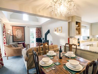 A dining table set with bowls plates glasses and cutlery beside a living area with sofas a wood stove and a kitchen in the background at South Lodge in Hazelbury Bryan