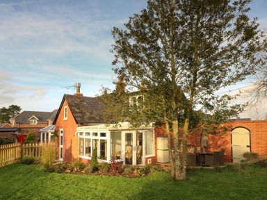 A brick house with a conservatory and garden furniture in a green yard at South Lodge in Hazelbury Bryan