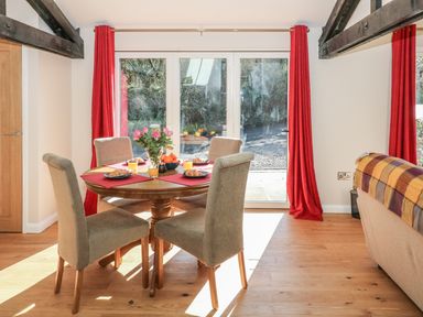 A dining area with a round wooden table set with croissants and juice four chairs and red curtains at Zeal Cottage in Crediton