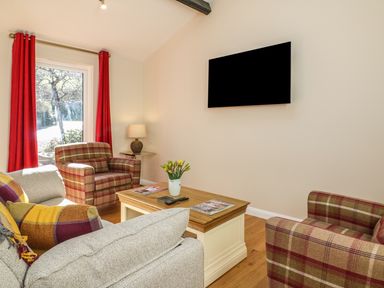 A living room with a sofa and armchairs around a coffee table with flowers and magazines at Zeal Cottage in Crediton