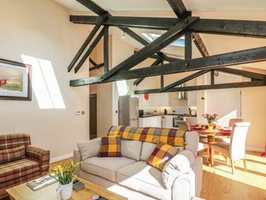A living room with sofas and a dining table with chairs under exposed wooden beams at Zeal Cottage in Crediton