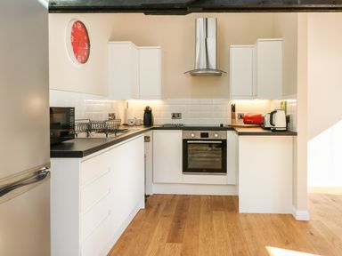 A kitchen with white cabinets and black countertops with appliances and wooden floor at Zeal Cottage in Crediton