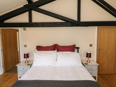 A bedroom with a bed white bedding red pillows wooden doors and two bedside tables with lamps at Zeal Cottage in Crediton