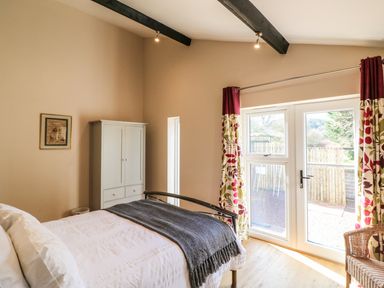 A bedroom with a bed white wardrobe floral curtains and glass door at Zeal Cottage Crediton