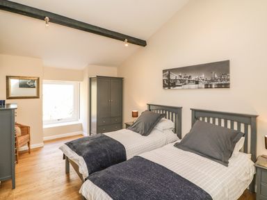 A bedroom with two single beds with dark headboards and bedding a wardrobe a chest of drawers and a window at Zeal Cottage in Crediton