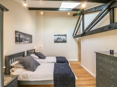 A bedroom with two single beds grey furniture wooden floor and black ceiling beams at Zeal Cottage in Crediton
