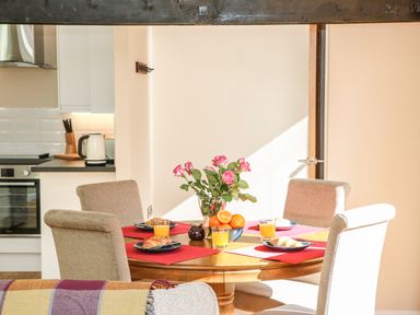A dining table set for breakfast with croissants orange juice a bowl of oranges and a vase of roses in a kitchen area at Zeal Cottage in Crediton