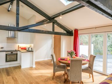A kitchen and dining area with wooden beams a round table with chairs and sliding glass doors at Zeal Cottage in Crediton