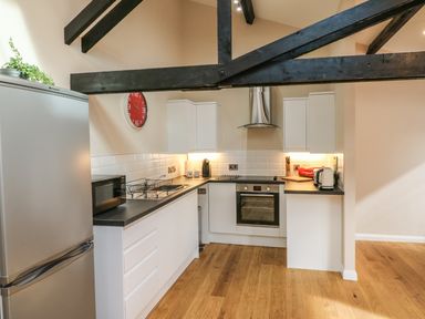 A kitchen with white cabinets black countertops wooden floor and exposed black ceiling beams at Zeal Cottage in Crediton