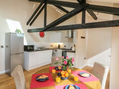 A kitchen with white cabinets a stainless steel fridge and a dining table set with croissants oranges and orange juice at Zeal Cottage in Crediton