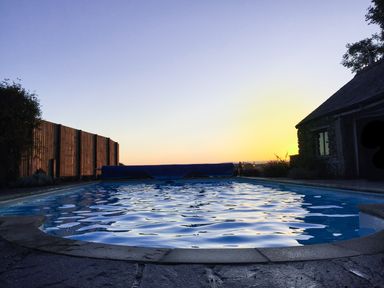An outdoor swimming pool with a wooden fence on the left and a stone building on the right at Pollys Bower in Landrake