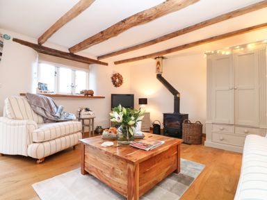 A living room with wooden ceiling beams a wood stove and a coffee table with flowers at Pollys Bower in Landrake
