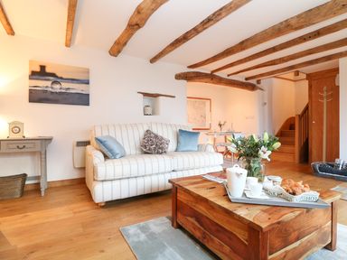A living room with a striped sofa and wooden coffee table with flowers and breakfast at Polly's Bower in Landrake