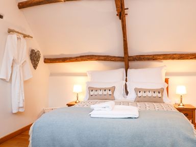 A bedroom with a double bed two bedside tables with lamps a bathrobe hanging on the wall and wooden beams at Polly's Bower in Landrake