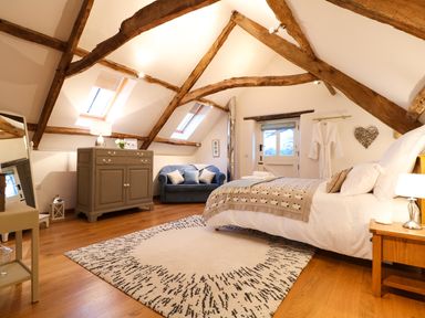 A bedroom with exposed wooden beams a bed a sofa a dresser a mirror and a rug at Polly's Bower in Landrake