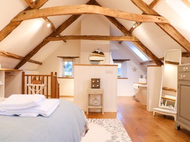 A bedroom with exposed wooden beams a bed with folded towels a wardrobe and a mirror at Polly's Bower in Landrake