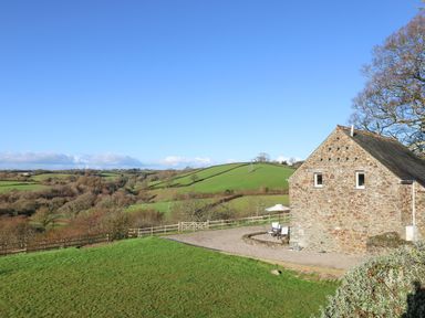 A stone house with outdoor patio furniture and green rolling hills in the background at Pollys Bower in Landrake