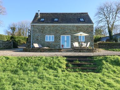 A stone house with outdoor chairs and an umbrella on a terrace surrounded by grass at Pollys Bower in Landrake
