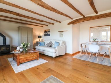 A living room with a striped sofa and wooden coffee table next to a dining table with white chairs at Pollys Bower in Landrake