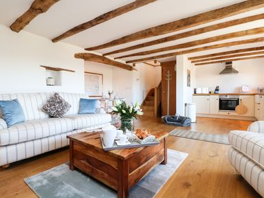A living room with wooden beams on the ceiling a striped sofa a wooden coffee table with a flower vase and tea set and an open kitchen at Polly's Bower in Landrake