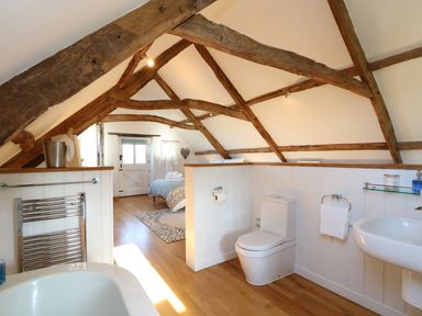 A bathroom with a toilet, sink, towel rack, and bathtub under exposed wooden beams at Polly's Bower in Landrake