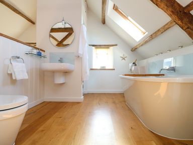 A bathroom with a toilet sink mirror bathtub wooden floor and exposed beams at Polly's Bower in Landrake
