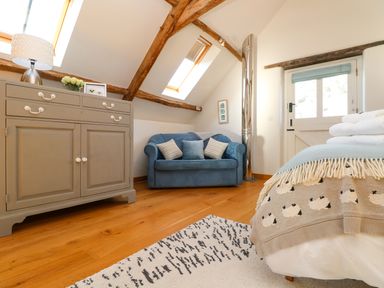 A bedroom with a blue sofa gray dresser wooden beams and a door at Polly's Bower in Landrake
