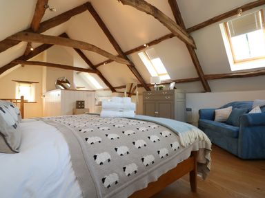 A bedroom with a bed covered by a sheep-themed blanket a blue sofa wooden beams on the ceiling and two skylight windows at Polly's Bower in Landrake