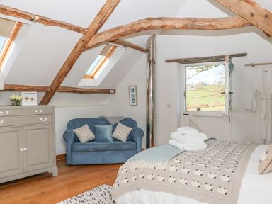 A bedroom with wooden beams a blue sofa a grey dresser and a bed with a blanket and towels at Pollys Bower Landrake