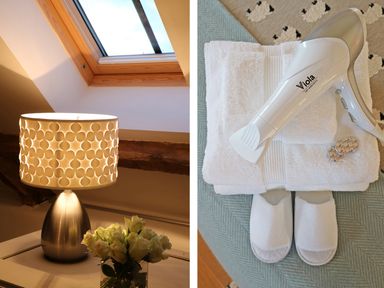 A table lamp with a patterned lampshade and a vase of white flowers under a skylight window and a hairdryer placed on folded white towels with white slippers on a textured surface at Polly's Bower in Landrake