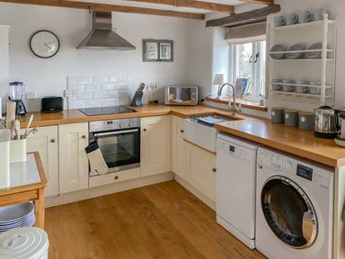 A kitchen with wooden countertops a washing machine dishwasher oven microwave and shelves with cups and plates at Pollys Bower in Landrake