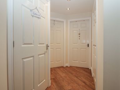 A hallway with four white paneled doors and wooden flooring at Y Enciliad in Rhosneigr