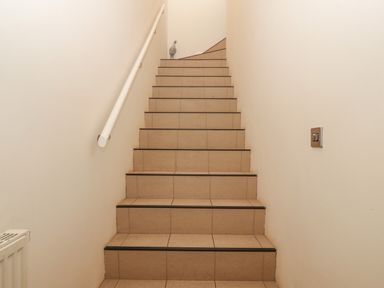 A tiled staircase with a white handrail on the left and a light switch on the right at Y Enciliad in Rhosneigr