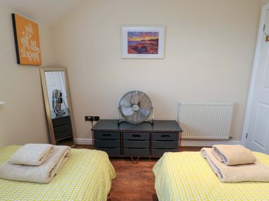 A bedroom with two single beds and a fan at Y Enciliad Rhosneigr
