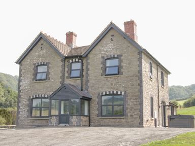 A stone house with two chimneys and dark framed windows surrounded by grass and trees at The Farm in Presteigne