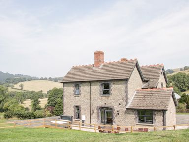 A stone house with a tiled roof and patio furniture in the countryside at The Farm in Presteigne