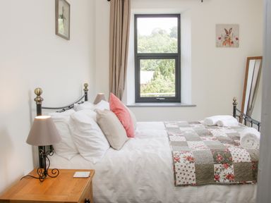 A bedroom with a bed covered in white linens and a patchwork quilt next to a wooden bedside table with a lamp at The Farm in Presteigne