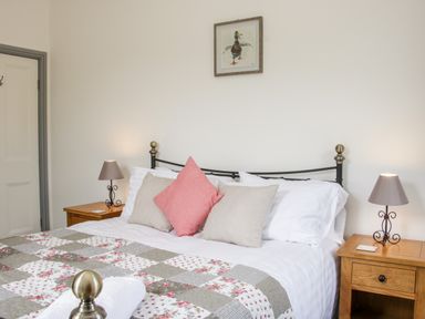 A bedroom with a bed with patterned quilt and pillows two wooden nightstands with lamps and a framed duck picture on the wall at The Farm in Presteigne