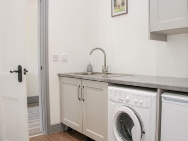 A laundry room with a washing machine under a countertop and a sink with a faucet at The Farm in Presteigne