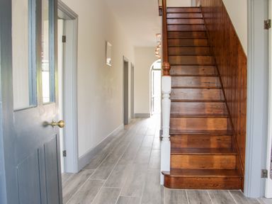 A hallway with wooden stairs and grey tiled floor at The Farm in Presteigne