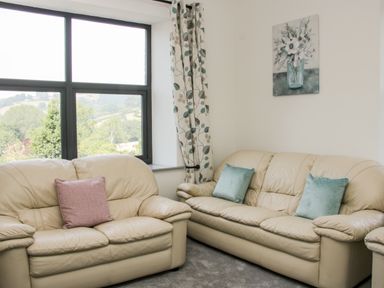 A living room with two beige leather sofas and a large window with curtains at The Farm in Presteigne