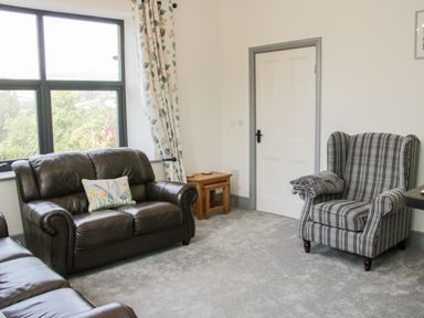 A living room with a brown leather sofa a striped armchair a door two side tables and window with leaf patterned curtains at The Farm in Presteigne