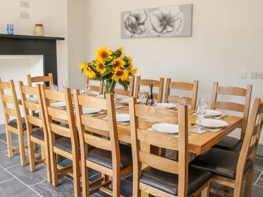 A wooden dining table with chairs plates glasses a bottle and sunflowers at The Farm in Presteigne