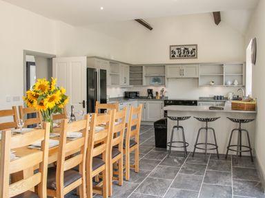 A kitchen with a long dining table with chairs and sunflowers a counter with stools and appliances at The Farm in Presteigne
