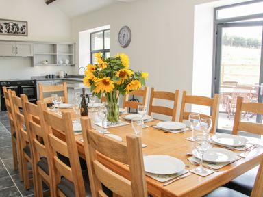 A dining room with a wooden table set with plates glasses and cutlery and a bouquet of sunflowers at The Farm in Presteigne