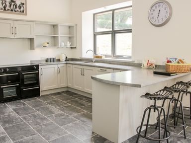 A kitchen with grey cabinets black stove two black stools and a large window at The Farm in Presteigne